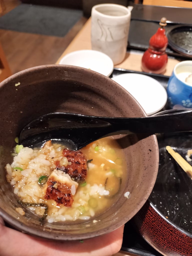 The transformation moment showing dashi being poured over the condiment-topped second serving, illustrating the ochazuke preparation that completes the hitsumabushi experience.